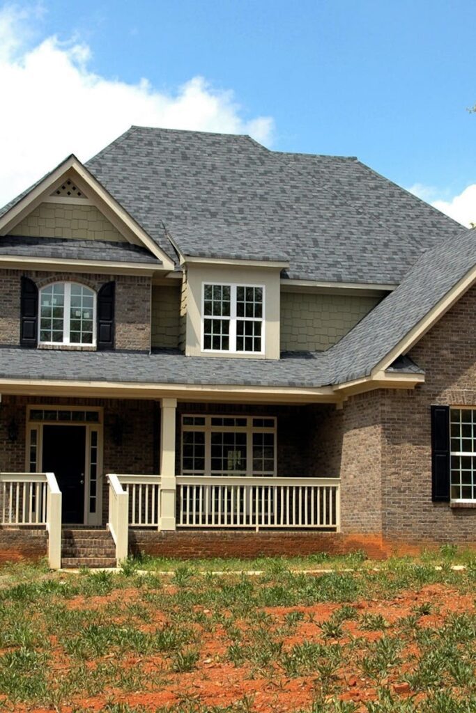 Classic two-story brick house with gable roof and front lawn in suburban setting.